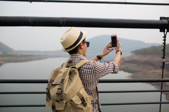 Young man using phone and selfie on bridge.