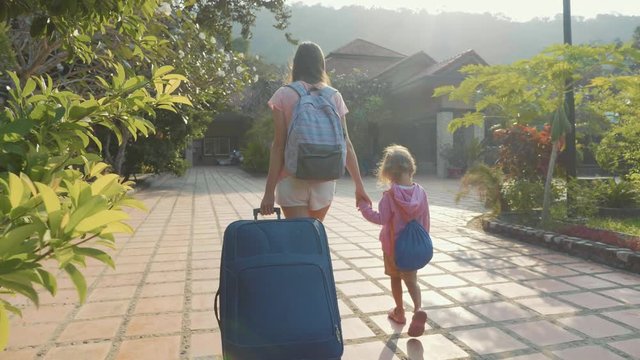 Young mother with daughter arriving at hotel, checking in, carrying luggage.