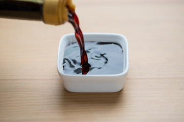 Close up pouring soy sauce in white bowl before eating food.