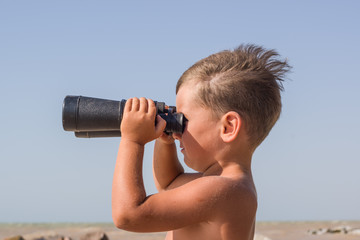 Tanned boy with binoculars against the stormy sea