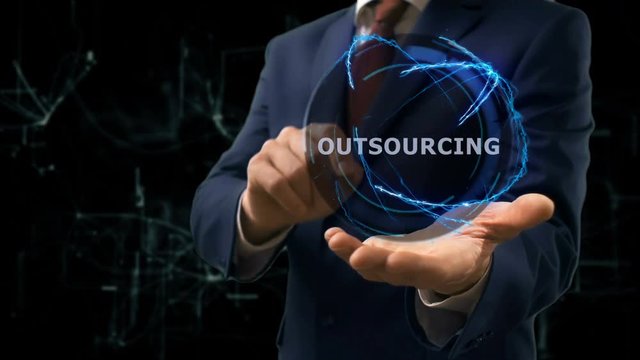 Businessman shows concept hologram Outsourcing on his hand. Man in business suit with future technology screen and modern cosmic background