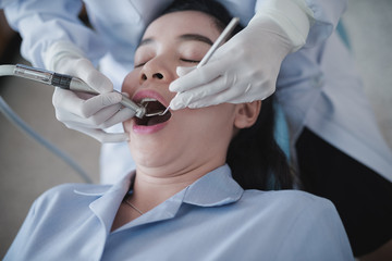 Hands of dentist holding a dental tool. Checking the teeth to the woman lying in the dental chair in a hospital.