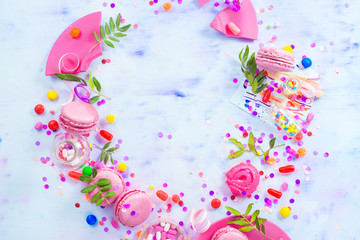 Obraz na płótnie Canvas Pink macarons, candies, confetti and sprinkles in a creative party vignette with copy space. Colorful celebration flat lay.