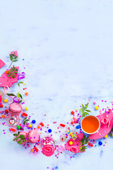 Colorful celebration flat lay with party supplies, confetti and sweets. Pink macarons with tea cup and shards of broken tea saucer with copy space.