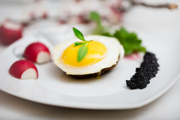 Meatball and egg on with black caviar on white plate