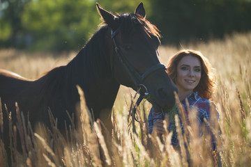 Portrait of a young woman and horse in the meadow at sunny summer