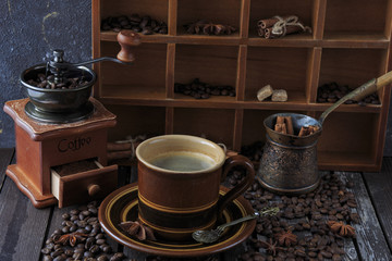 on a dark wooden table a cup of coffee, a coffee grinder and coffee beans