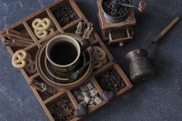 on a dark wooden table a cup of coffee, chocolate and pretzels in a box, a coffee grinder