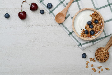 Top view mockup yogurt in wooden bowl with blueberries and cherry on the white stone.