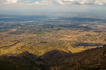 Fototapeta premium Top-down view on an american city under the mountain. Bright skyline with many white clouds, wide low-rise city on the horizon in the hot sunny day.
