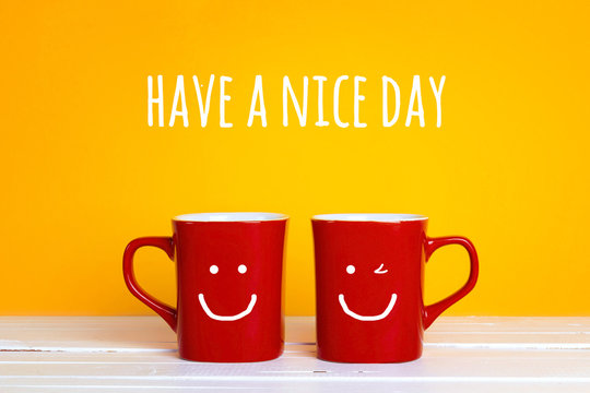 Two red coffee mugs with a smiling faces on a yellow background with the phrase Have s nice day