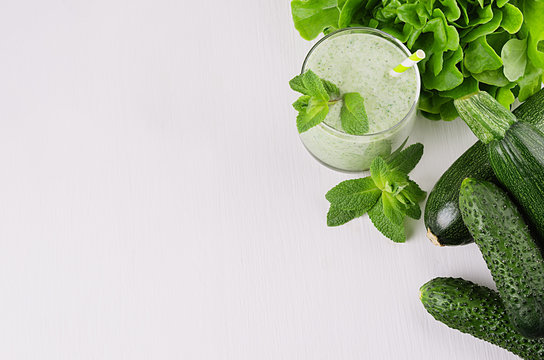 Healthy green spinach smoothies with leaf mint, greens, straw, green vegetables on white soft wood board, copy space, top view.