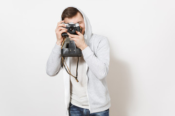 Young handsome smiling man student in t-shirt and light sweatshirt with hood with headphones takes pictures on retro camera with cover isolated on white background. Concept of photography, hobby