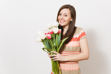 Beautiful young happy brunette woman in light patterned dress is holding bouquet of white and pink tulips in hands, smiling and rejoices in studio on white background. Concept of holiday, good mood.