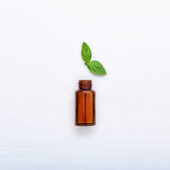 Bottle of essential oil with fresh basil leaves setup with flat lay on white wooden table.