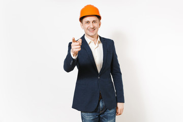Young handsome successful smiling businessman in dark suit, protective hardhat pointing index finger on camera isolated on white background. Male worker for advertisement. Business, working concept.