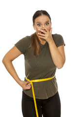 Shocked young woman measuring her waist on white background