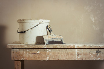 Scene of apartment repair. A bucket with putty and a putty knife on a wooden stand