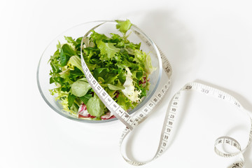 Close up green vegetables salad in glass bowl, tailor measuring tape isolated on white background. Proper nutrition, vegetarian food, healthy lifestyle, diet meal. Diabetes dieting concept. Copy space