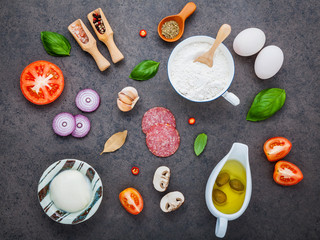 The ingredients for homemade pizza with ingredients sweet basil ,tomato ,garlic ,bay leaves ,pepper ,onion and mozzarella cheese on dark stone background with flat lay.