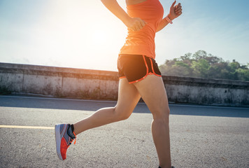 An asian woman athletic is jogging on the concrete road, she is warming her body and tideten her tying her shoes tightly fitting before workout.