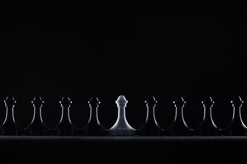 silhouettes of black and white chess pawns isolated on black, business concept