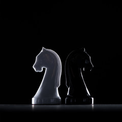 silhouettes of white and black chess knights isolated on black, business concept © LIGHTFIELD STUDIOS