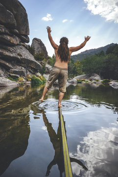 Back view of slackliner with drealocks practicing slack line over the water in a lake in La Pedriza, Spain