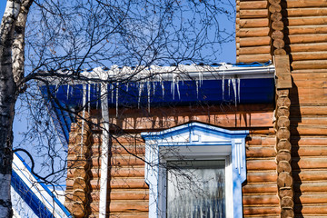 Icicles hanging from the roof of a beautiful wooden house made of logs, rustic style, spring landscape. The concept of the danger of snow melt due to poor insulation