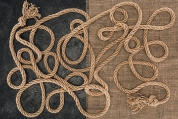 flat lay with brown marine ropes with knots on sackcloth and dark concrete surface
