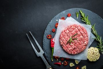 Organic raw ground beef patties for making homemade burgers with rosemary, species and carving fork...