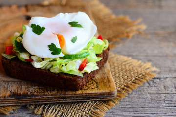 Egg poached sandwich. Egg poached on rye bread slice with fresh vegetable salad. Healthy sandwich photo. Wooden background. Rustic style. Closeup