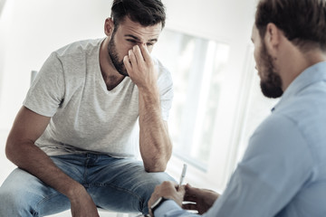 Personal problems. Nice handsome unhappy man holding his nose and feeling upset while thinking about his problems