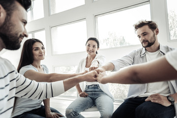 Team spirit. Positive happy joyful people sitting together and showing their unity while smiling to...