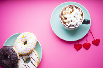 Freshly brewed cup of coffee with marshmallow, donuts and sweets on the pink background. Gifts with ribbon and hearts. Top view. Space for your text.