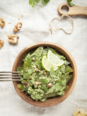 Green peapods with pesto sauce in wooden bowl on rustic background.