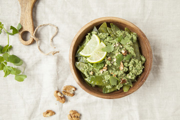 Green peapods with pesto sauce in wooden bowl on rustic background.