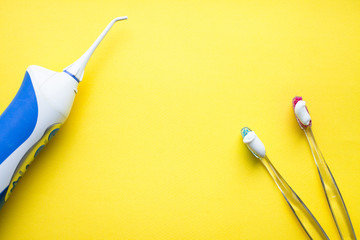 Irrigator and tooth brushes on the yellow background. Top view. Space for your text.