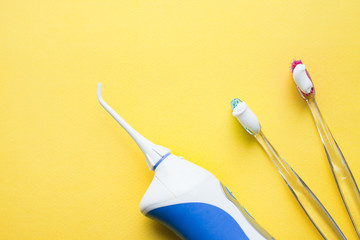Irrigator and tooth brushes on the yellow background. Top view. Space for your text.