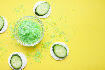 Skin treatment with cucumber and green sea salt on the yellow background. Space for your text. Top view.