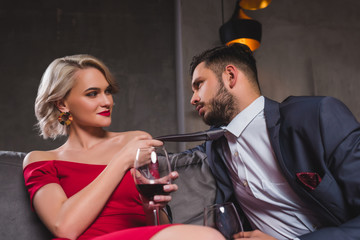 seductive young couple drinking wine, woman holding necktie of handsome boyfriend
