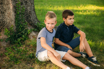 Fototapeta premium Two children are playing in the park. Two beautiful boys in T-shirts and shorts have fun smiling. They eat ice cream, jump, run. Summer is sunny