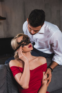 handsome man looking at beautiful sensual woman in red dress and black lace mask