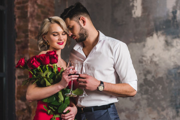 seductive young couple drinking red wine, woman holding beautiful roses