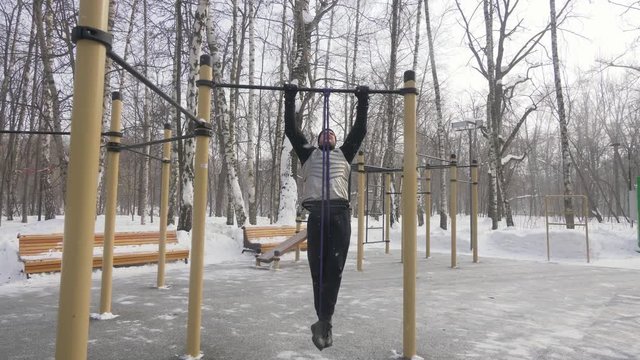 Fitness man training pull up exercise on sport ground. Outdoor winter training