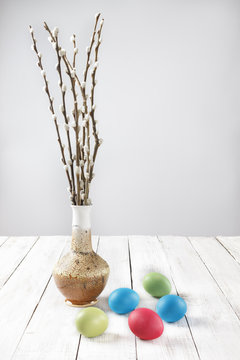 Branches of willows in a vase and dyed Easter eggs on a white wooden table.