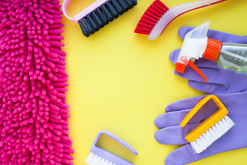 Cleaning Concept. Set of yellow, green, blue, red, white and pink cleaning tools: rags, sponges, brushes, dishwashing liquid, rubber gloves on the yellow background, top view, flat lay, close up