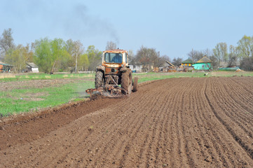 Obraz premium Tractor plowing field and white stork. Rural landscape.