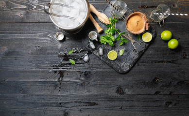 Cocktails ingredients with coconut sugar in coconut shell, Metal ice bucket, old scissors on marble board on black rustic table, Mojito, alcoholic, non-alcoholic drink-beverage. Top view, copy space
