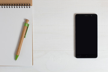 Pen of a natural wood smartphone and notebook on a white table.